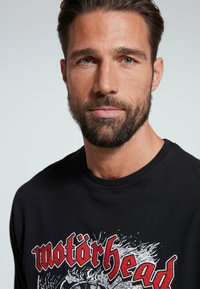 Černá mikina s výrazným grafickým designem "Motörhead" v červené a bílé barvě. Měkká látka, kulatý výstřih a ribbované manžety.