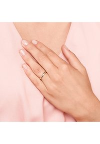 Hand mit heller Hautfarbe, die auf pinkem Stoff ruht und einen schlichten goldenen Damenring am Ringfinger trägt.