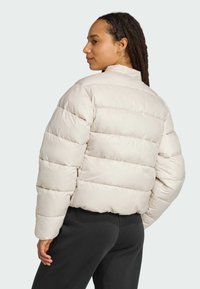 A woman with natural hair wears a light beige puffer jacket, facing slightly to the side against a plain background.