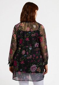 Durchsichtige schwarze Bluse mit floralem Muster in Pink, Lila und Grün. Lange Ärmel, abgerundeter Saum und geraffte Taillenpartie.