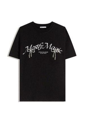 T-shirt nera in cotone con la scritta "Mostly Magic" in bianco, decorata con perle. Maniche corte, vestibilità rilassata, collo a giro.