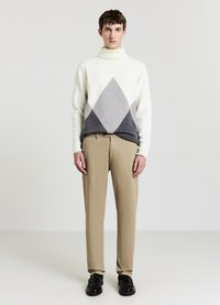 Maglione a collo alto lavorato a maglia color crema con motivi a diamante grigi e grigio scuro, abbinato a pantaloni beige e scarpe nere. Tessuto liscio.