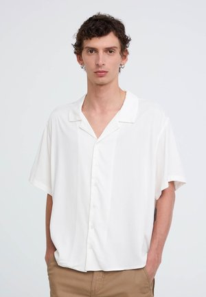 Camicia bianca a maniche corte con colletto, realizzata in un tessuto morbido e leggero, con una vestibilità rilassata. Leggera lucentezza e dettagli minimali.