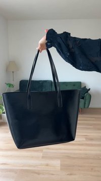 Zwarte leren tote bag met twee lange handvatten, gestructureerde vorm, gladde textuur, minimale hardware en geen zichtbare logo's of patronen.