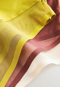 Couches de tissu en maille transparente jaune, marron et blanche avec des bords d'ourlet solides qui se chevauchent sur une surface plane.