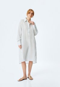 Abito lungo, leggero e bianco con righe verticali, allacciatura con bottoni e maniche con polsini. Presenta bottoni laterali e una vestibilità rilassata.