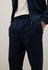 Pantaloni sportivi blu navy realizzati in un tessuto liscio con fascia in vita elastica e tasche laterali, caratterizzati da una vestibilità affusolata e linee pulite.