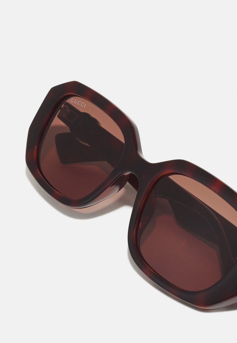 Lunettes de soleil en écaille de tortue brune avec des montures hexagonales surdimensionnées, dotées de verres foncés et d'un logo discret en haut à gauche.