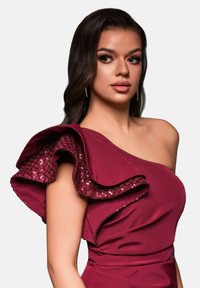 Robe bordeaux à une épaule avec un accent de volants superposés ornés d'un motif pailleté. Confectionnée en tissu lisse, au design ajusté.