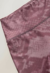 Nahaufnahme eines violetten und mauvefarbenen gemusterten Stoffes mit einem kleinen kreisförmigen Punktmuster und sichtbaren Nahtstichen.