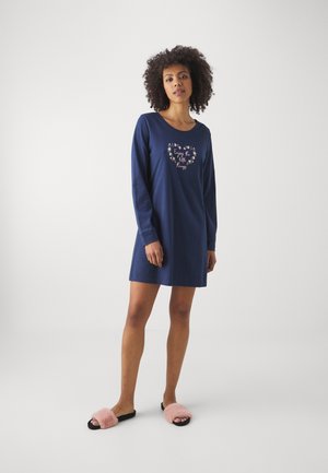 Nuit en jersey bleu marine à manches longues avec un col rond et une broderie de cœur floral. Le modèle porte des chaussons roses duveteux. Design simple et décontracté.
