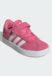 Zapatilla de ante rosa con diseño de tres franjas blancas, suela de goma, collar acolchado y tira de Velcro. Presenta una parte superior texturizada y puntera reforzada.