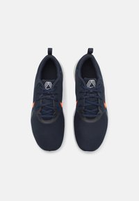 Baskets de sport bleu marine avec un matériau en maille, accents gris, logo orange et semelle grise. Comprend des lacets et un col rembourré.