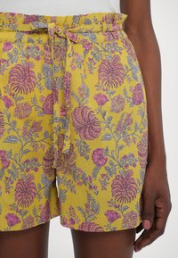 Pantaloni corti floreali con una base gialla e motivi di fiori rosa e grigi, cintura in tessuto e design dalla vestibilità rilassata.