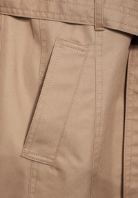 Tela de algodón beige con un bolsillo plano, costuras visibles y una textura lisa, con un diseño ligeramente estructurado.