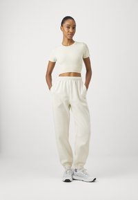 Hvit kortermet t-skjorte i ribbestrikket tekstur, kombinert med lyse beige joggebukser med elastisk midje og mansjetter.