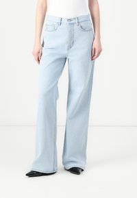 Lyseblå, vide jeans med høy midje, laget av denim. Har klassisk fem-lommers stil og metallknappåpning foran.