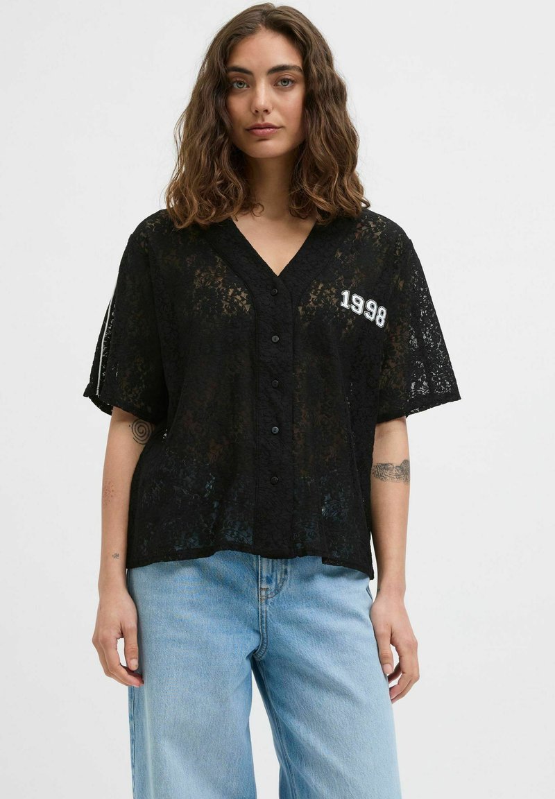 Camisa de encaje negra con escote en V, mangas cortas y cierre de botones. Presenta el año "1998" bordado en blanco en contraste. Textura ligera.