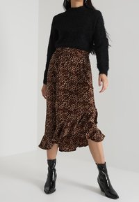 Svart fluffig tröja parat med en brun leopardmönstrad midi-kjol med volang i fållen, bärs med glänsande svarta ankelstövlar.