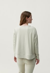 Ljusgrå oversized sweatshirt med rund halsringning, sänkta axlar och mjukt tyg. Har en hög-låg nederdel och avslappnad passform.