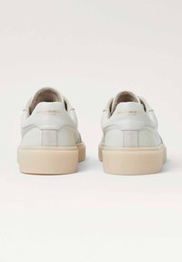 Weiße Ledersneaker mit glatter Textur, runder Zehenpartie, beiger Gummisohle und dezenter goldener Markierung an der Ferse.
