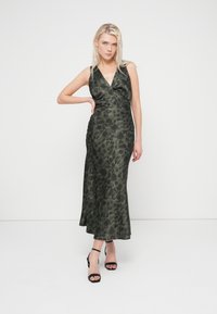 Sleeveless olive green floral dress in satin with a plunging neckline and a fitted silhouette, featuring a side slit and flowing hemline.