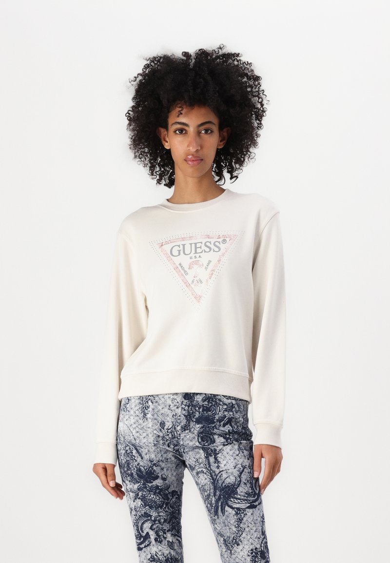 Crème sweatshirt met een driehoekig logo in roze en grijs; gecombineerd met blauwe legging met een patroon van bloemen en vogels.