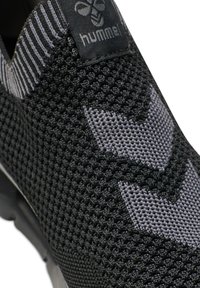 Black and gray sneaker with a textured mesh upper, featuring a logo patch and angular pattern accents. Slip-on design with a flexible sole.
