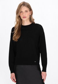 Maglione nero a maniche lunghe realizzato in un materiale a maglia leggero e trasparente. Presenta un collo rotondo e un orlo a costine, con un piccolo logo in evidenza in basso.