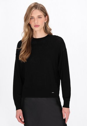 Zwarte lange mouwen sweater van een lichte, doorschijnende breimateriaal. Heeft een ronde halslijn en een geribde zoom, met een klein logo accent aan de onderkant.