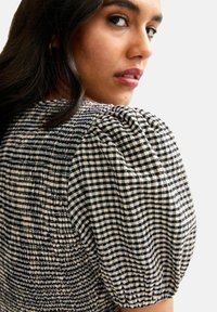 Black and white checkered top with puffed sleeves. The texture features smocking and a soft fabric, designed for a fitted silhouette.