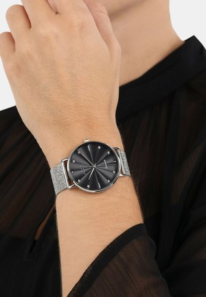 Silberne Mesh-Armbanduhr mit schwarzem Zifferblatt, das radiale Linien, silberne Stundenmarkierungen und ein rundes Gehäuse aufweist.