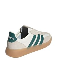 Sneaker Adidas a bassa con nastro bianco, strisce e dettagli del tallone verdi, accenti in suede beige e suola in gomma color caramello.