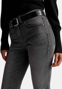 Vaqueros de mezclilla gris con una silueta ajustada, con detalles de costura sutil y un cinturón negro con patrón de cocodrilo. Tejido texturizado.