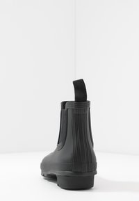 Botte noire en caoutchouc à la cheville avec un design texturé, des panneaux élastiques sur les côtés et une languette à l'arrière pour un enfiler facile.