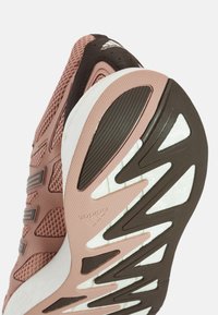 Baskets de sport roses et brunes présentant une tige en mesh texturé, une semelle en caoutchouc distinctive avec des rainures et des accents blancs sur la semelle intermédiaire.