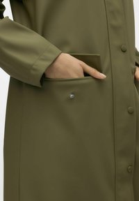 Olivno zelena vodoodporna jakna z ohlapnim krojem, zapiranjem na pritrdilne gumbe in stranskimi žepi z okrasnim detajlom na gumbih. Gladka tekstura.