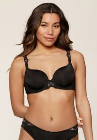 Soutien-gorge noir matelassé avec des accents en dentelle et de la broderie florale sur les bretelles. Tissu lisse, conception avec armatures et fermeture à crochets au dos.