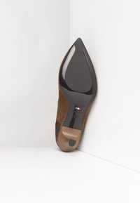 Scarpa con tacco alto in suede marrone, con punta appuntita, caratterizzata da un motivo rettile in rilievo sul tacco e una suola nera liscia.