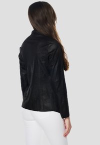 Melnā ādas jaka ar pieguļošu dizainu, gludu tekstūru un garām piedurknēm, kombinēta ar baltām džinsa biksēm.