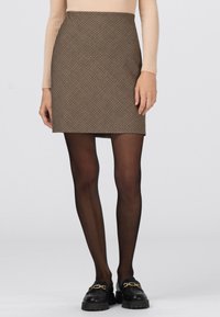 Bruine minirok met patroon en een getailleerd ontwerp, gecombineerd met doorschijnende zwarte panty's en grove zwarte loafers met gouden accenten.