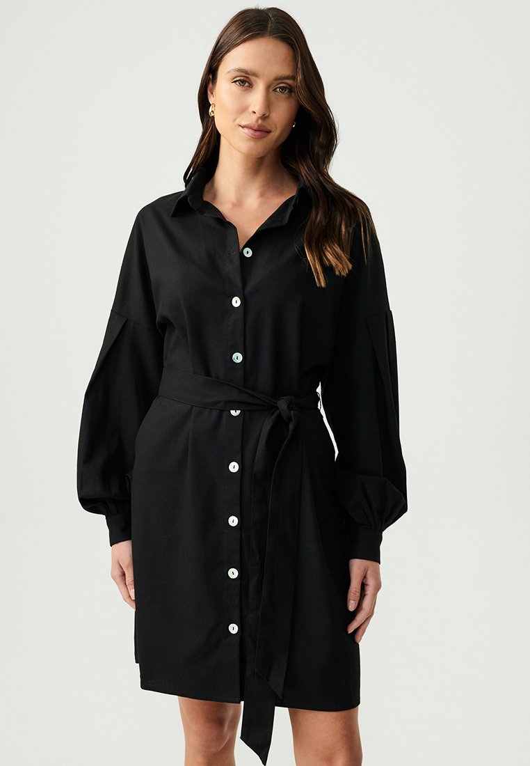 Vestito nero con bottoni, realizzato in tessuto morbido, caratterizzato da maniche lunghe, una vita con lacci e bottoni bianchi lungo la parte anteriore per la chiusura.