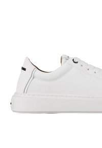 Sneaker in pelle bianca con tomaia strutturata, punta tonda, suola di gomma spessa e design minimalista. Presenta occhielli neri e un branding discreto.