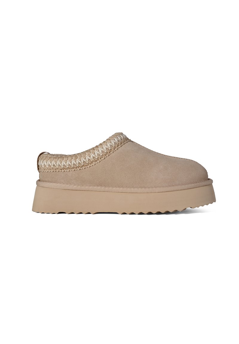 Beige suede klompen met een structuur crème gevlochten accent rond de kraag, en een dikke beige rubberen zool met een zaagtandprofiel.