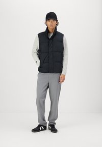 Vest negru căptușit, pulover texturat gri, pantaloni gri și sneakers negri cu dungi albe. Design simplu și paletă de culori neutră.