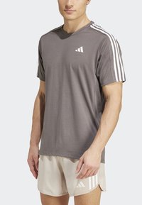 Camiseta deportiva gris de manga corta, con tres franjas blancas en los hombros y un pequeño logotipo blanco en el pecho.