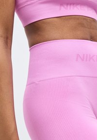 Γυμνασμένη μέση και μπράτσο που φοράει ροζ αθλητικό μπουστάκι Nike χωρίς ραφές και κολάν με ψηλή μέση, σετ με λεπτομέρειες λογότυπου.