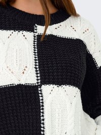 Gruby sweter z dzianiny z czarno-białym w kratę wzorem, z teksturowanymi detalami kabla i okrągłym dekoltem. Lekki i przytulny.