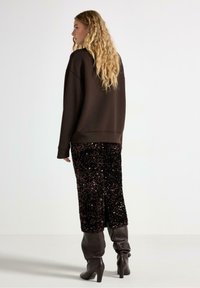 Brun oversized sweatshirt, svart paljetterad pennkjol, knähöga bruna stövlar med slouch. Strukturerade ytor, subtil glans på kjolen.