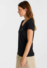 Zwart V-hals T-shirt met korte mouwen, gemaakt van zachte stof, met een subtiel logo aan de linkerkant. Eenvoudige, ontspannen pasvorm.